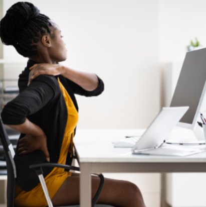 Trabalhadora sentada em frente ao computador com dor nas costas